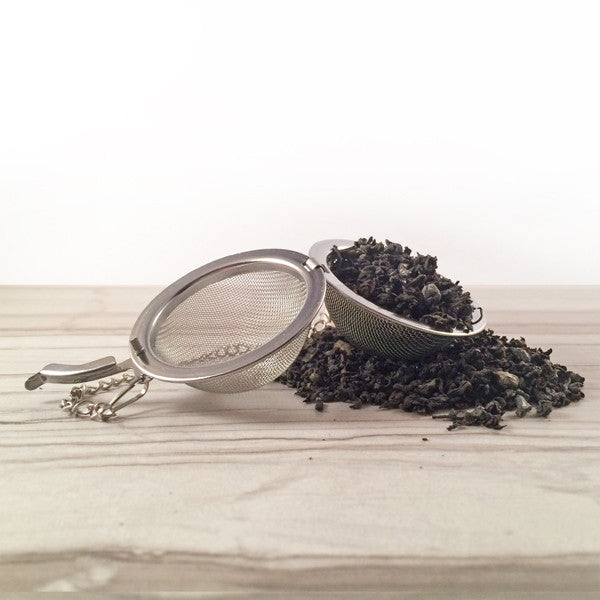 Black tea on while tile spilling out of tea ball, Dembones